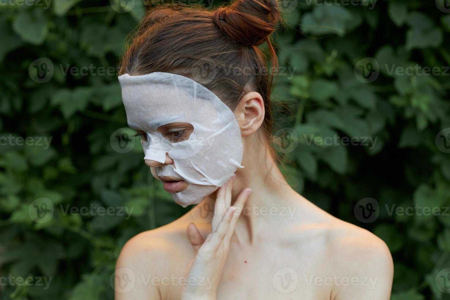 Portrait of a girl face mask Looks down and holds his hand near his neck bare shoulders bushes in the background photo