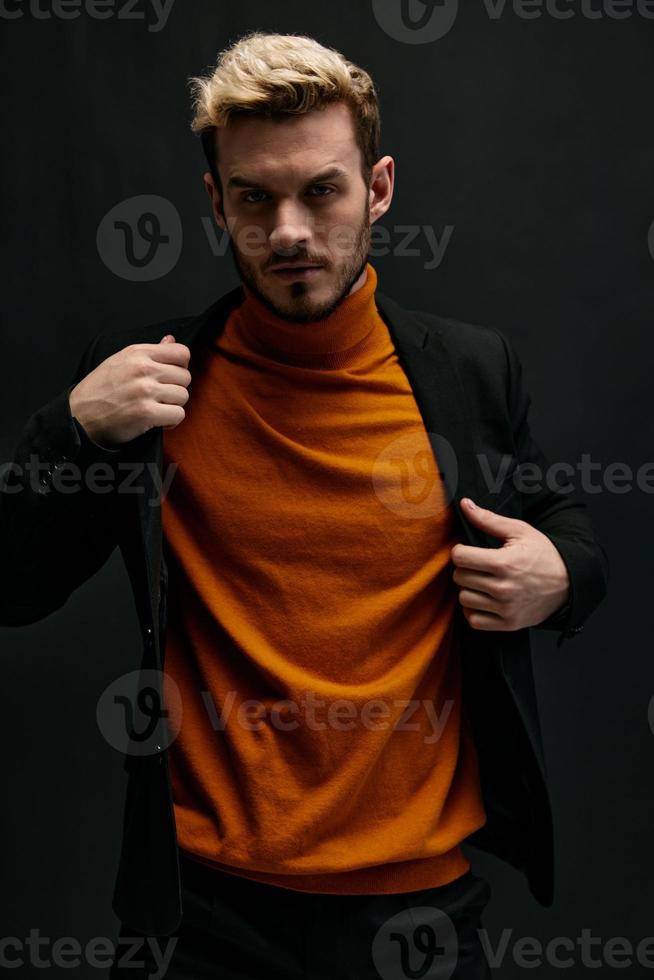 un hombre en un naranja suéter y un chaqueta en un oscuro antecedentes rubio retrato de cerca foto