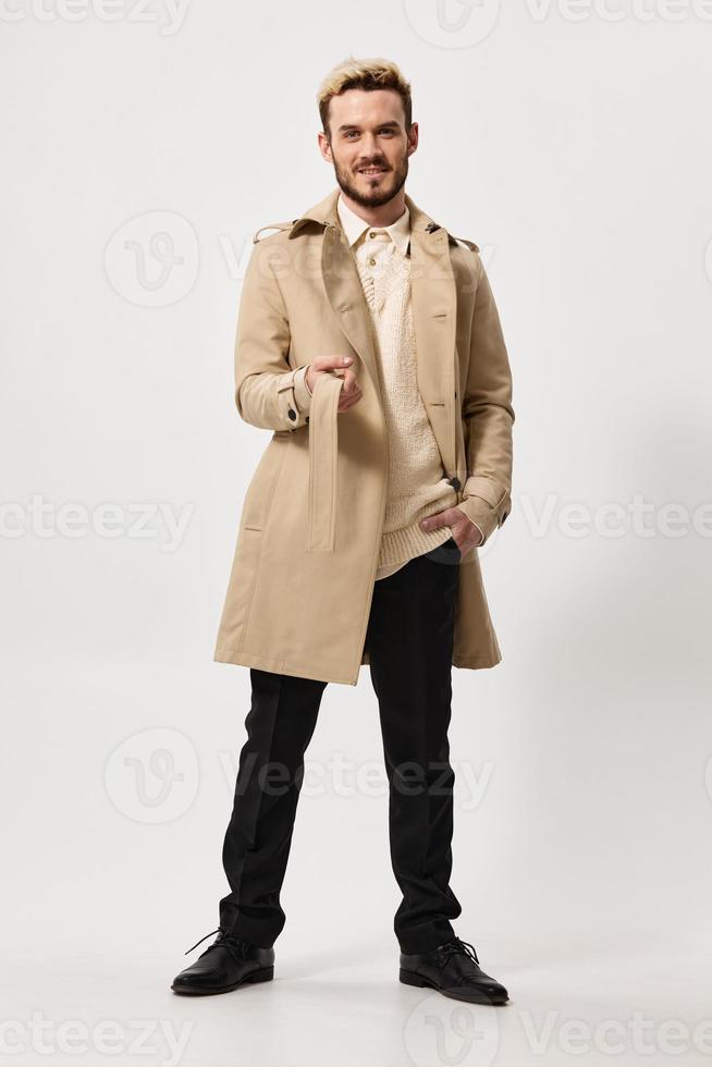 a man in a dark coat and trousers walks to the side on a light background trend of the season model photo