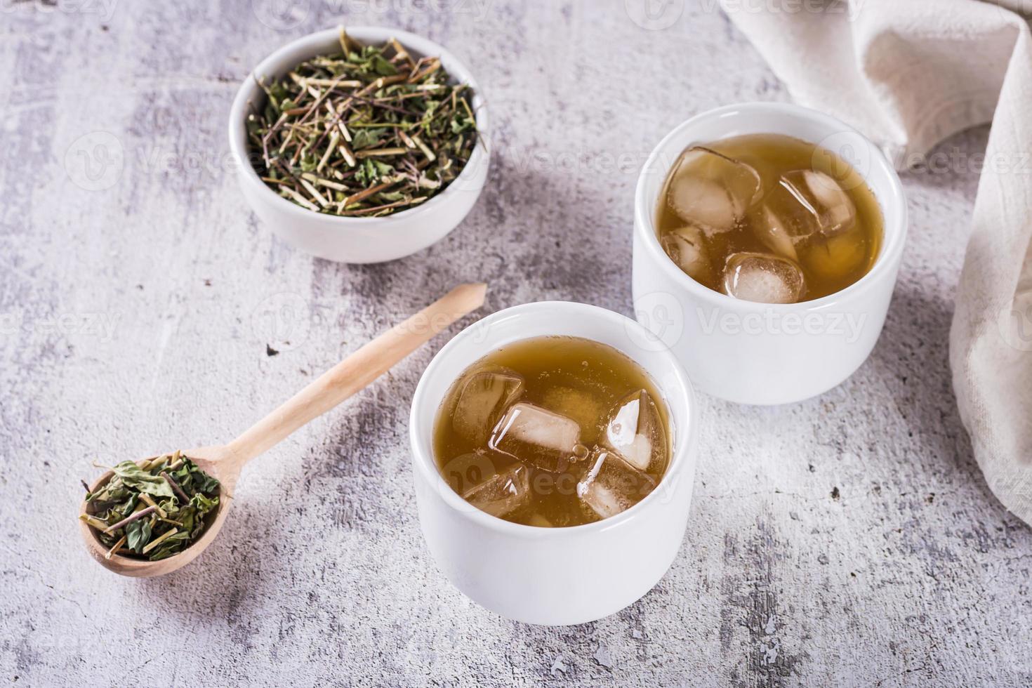 con hielo verde japonés hojicha té en tazas y hojas en un cuenco en el mesa foto