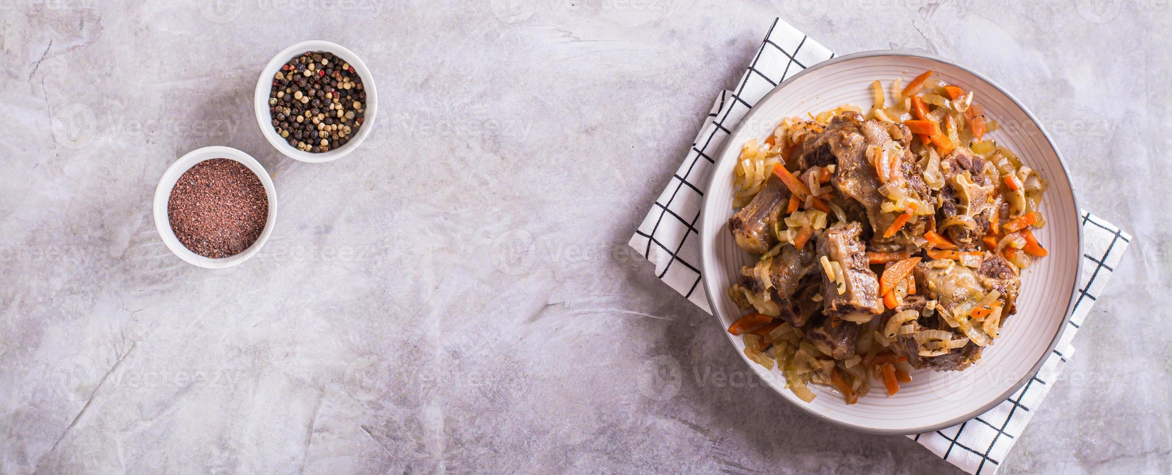 Stewed beef oxtail with wine and vegetables on a plate on the table top view web banner photo