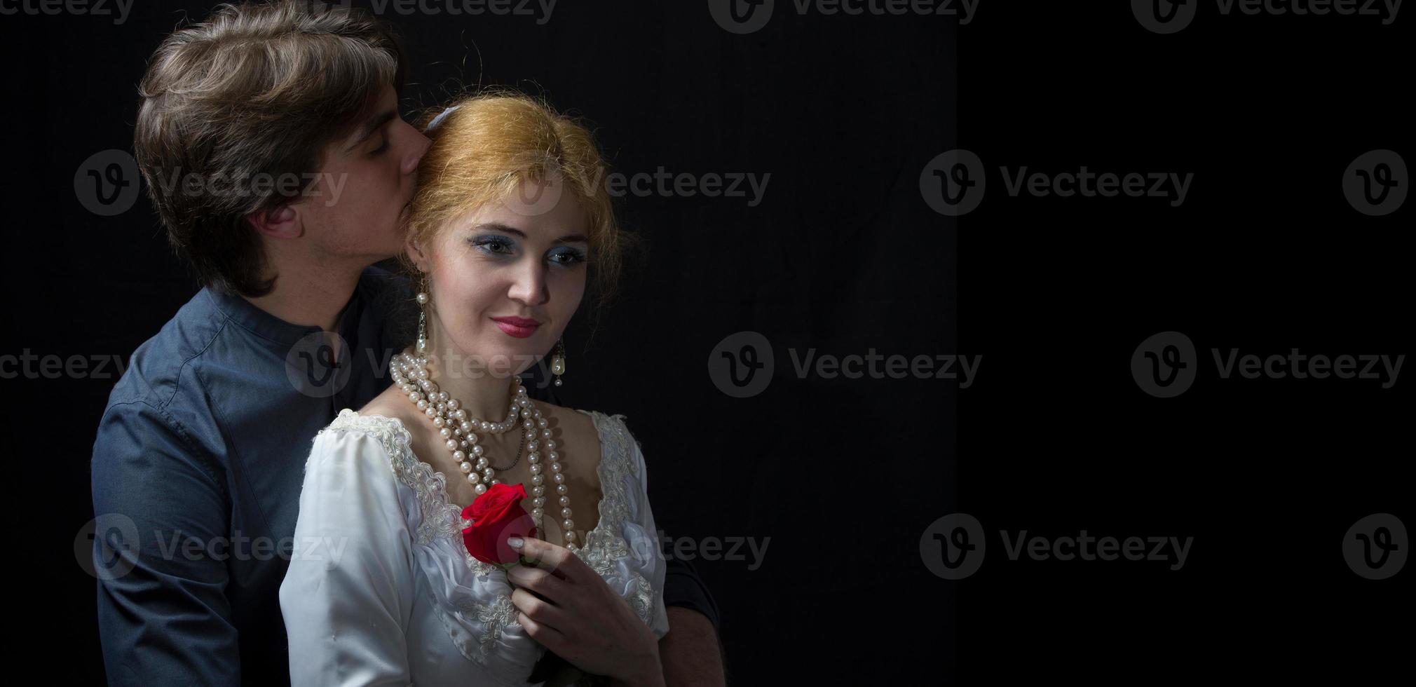 hermosa Pareja en retro estilo. un hombre abrazos un mujer. niña en un blanco vestir con un rojo Rosa en un antecedentes de un hombre. foto