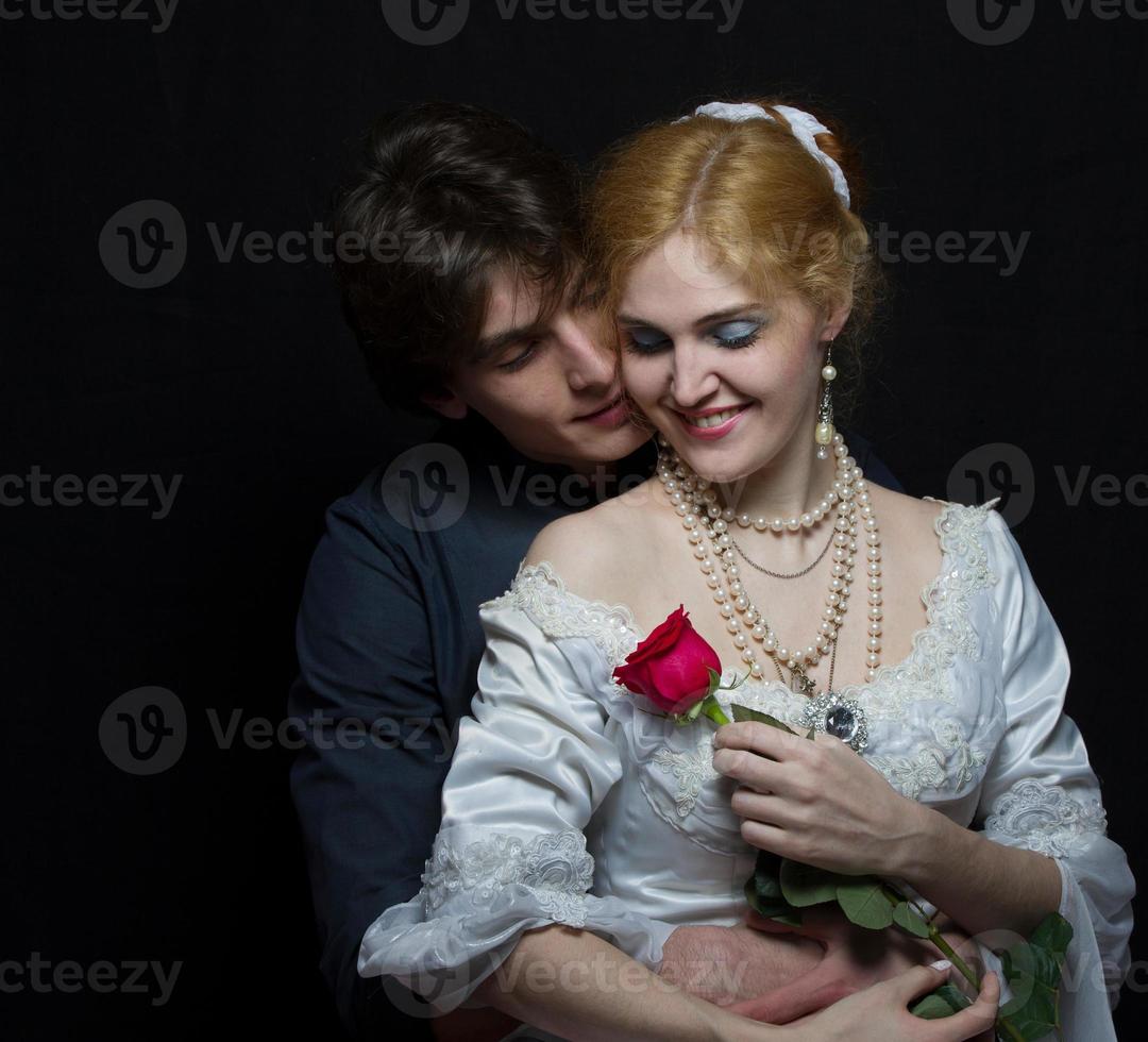 Beautiful couple in retro style. A man hugs a woman. Girl in a white dress with a red rose on a background of a man. photo