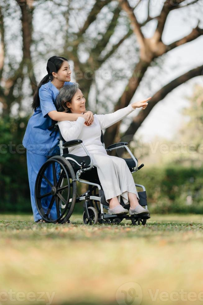 Elderly asian senior woman on wheelchair with Asian careful caregiver and encourage patient, walking in garden. with care from a caregiver and senior health insurance. photo