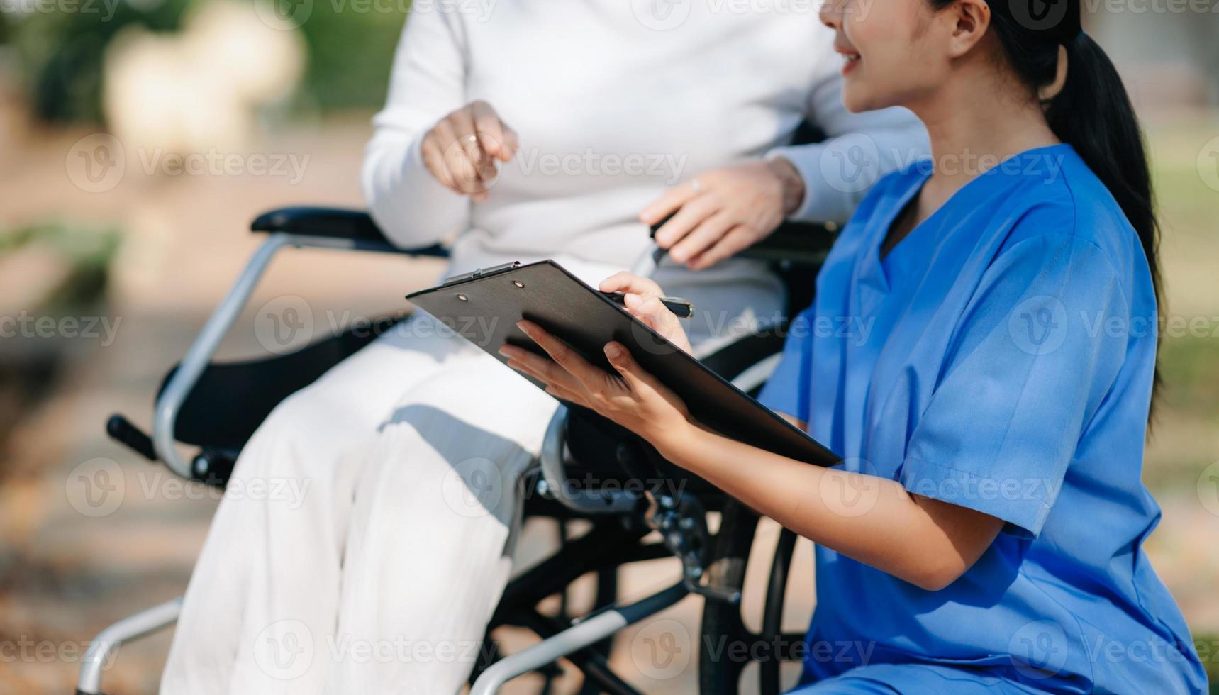 Asian careful caregiver or nurse and the happy patient in a wheelchair are walking in the garden. to help and encourage and rest your mind with green nature. Use a stethoscope to listen to your photo