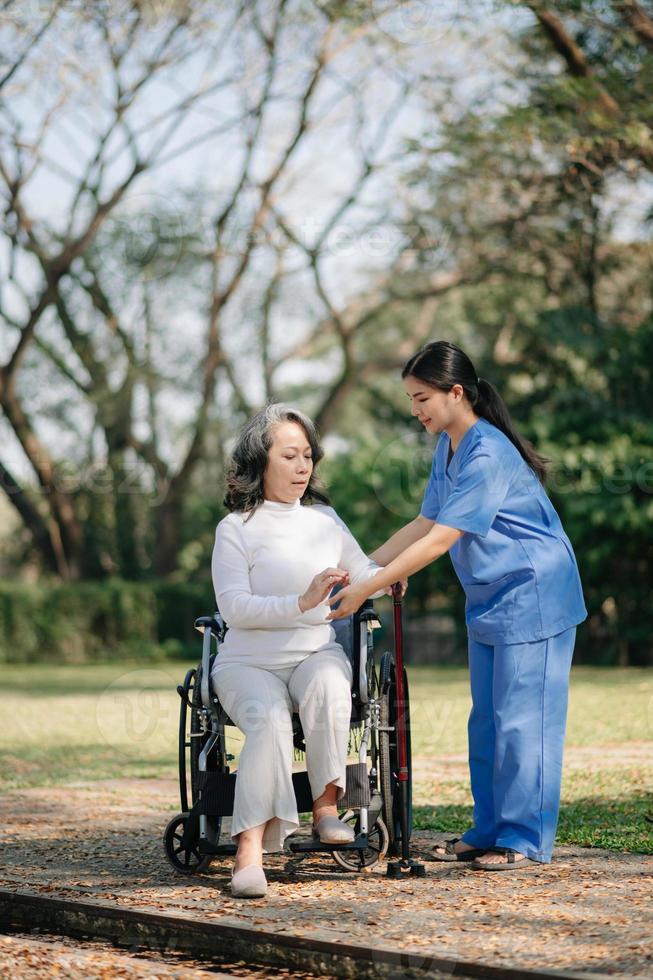 Elderly asian senior woman on wheelchair with Asian careful caregiver. Nursing home hospital garden concept. photo
