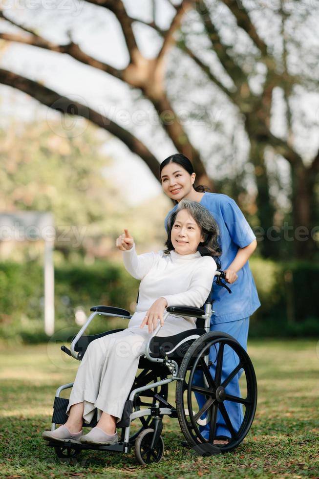 mayor asiático mayor mujer en silla de ruedas con asiático Cuidado cuidador y animar paciente, caminando en jardín. con cuidado desde un cuidador y mayor salud seguro. foto