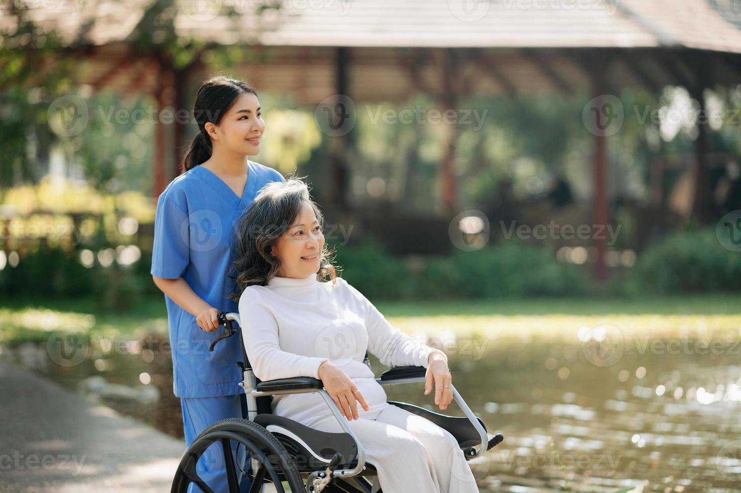 mayor asiático mayor mujer en silla de ruedas con asiático Cuidado cuidador y animar paciente, caminando en jardín. con cuidado desde un cuidador y mayor salud seguro. foto