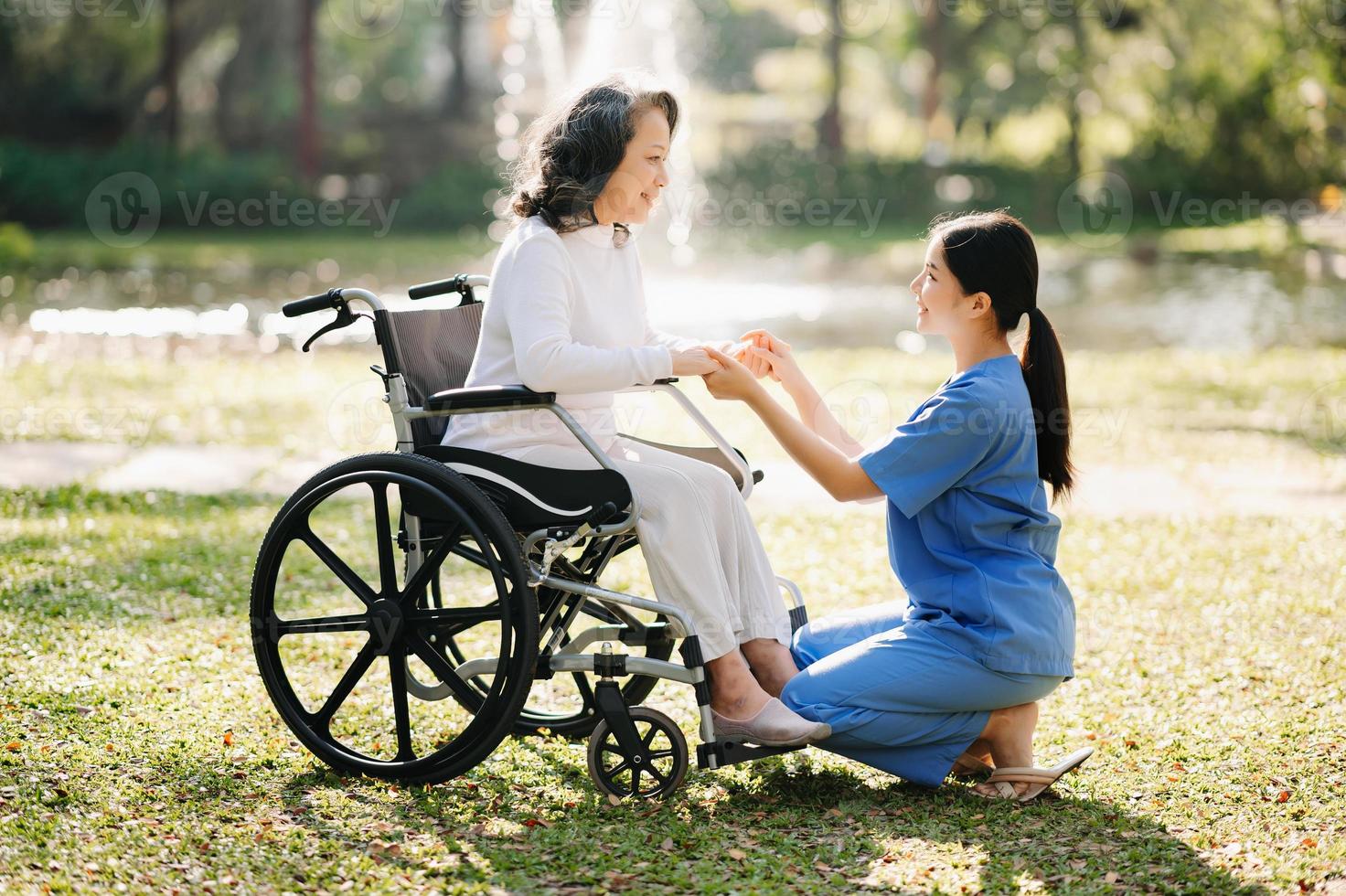 Elderly asian senior woman on wheelchair with Asian careful caregiver. Nursing home hospital garden concept. in sun light photo