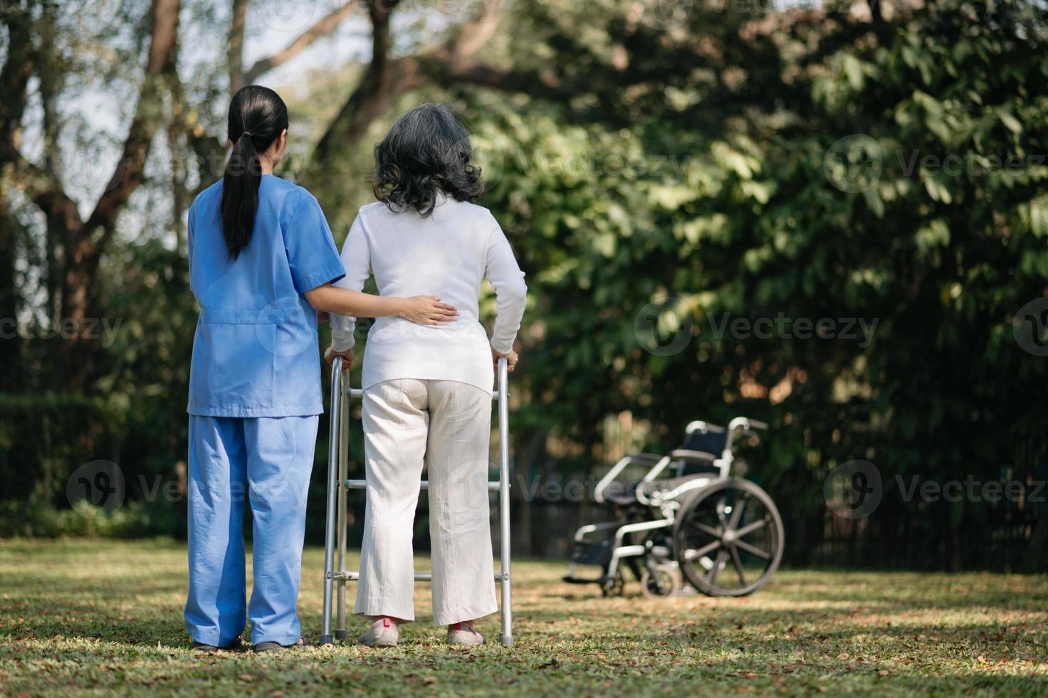 Asian careful caregiver or nurse and the happy patient in a wheelchair are walking in the garden to help and encourage and rest your mind with green nature. Help support yourself to learn to walk. photo