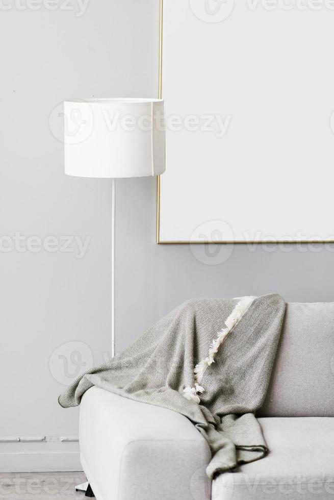 Stylish minimalistic interior of the living room in gray. Sofa with plaid, floor lamp and mockup white frame on the wall photo