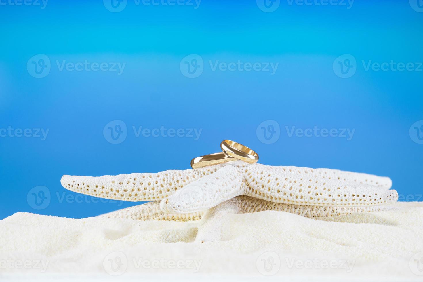 Wedding golden rings on white starfish on sandy beach. Marine decor with accessories for tropical wedding ceremony on summer background in hot country. Travel, relax, honeymoon photo
