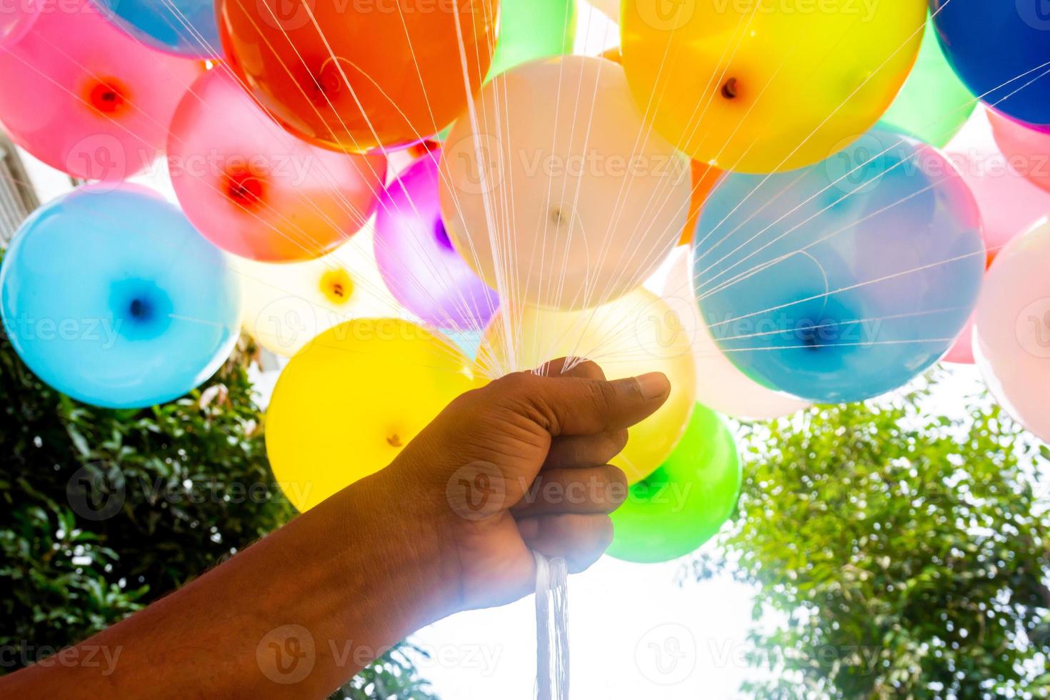 A fistful of hands is holding a bunch of colored gas-filled balloons. Colorful balloons background. photo