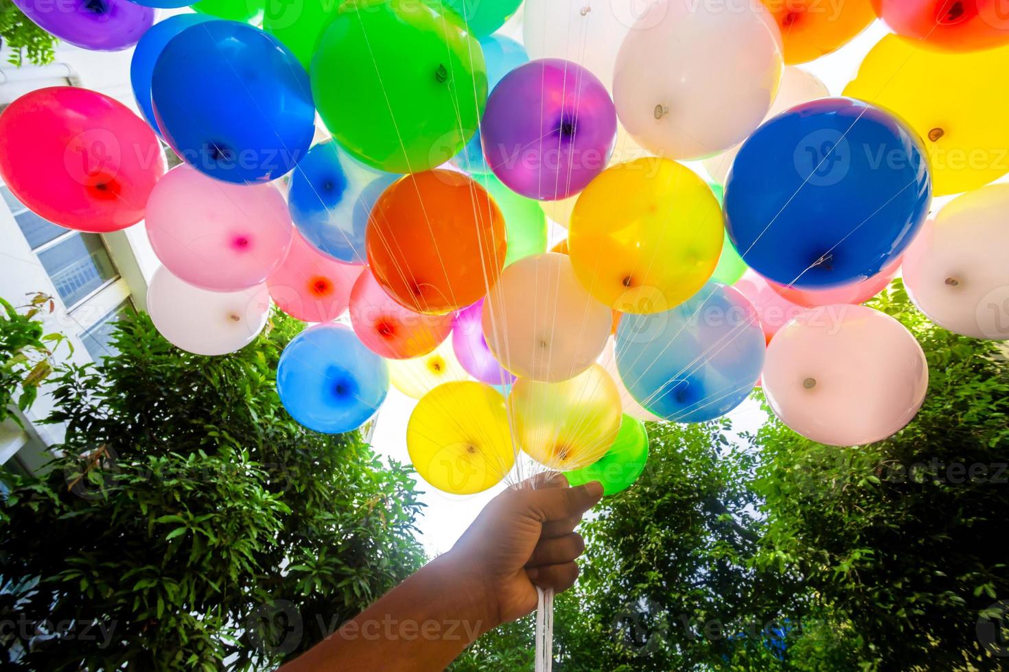 A fistful of hands is holding a bunch of colored gas-filled balloons. Colorful balloons background. photo