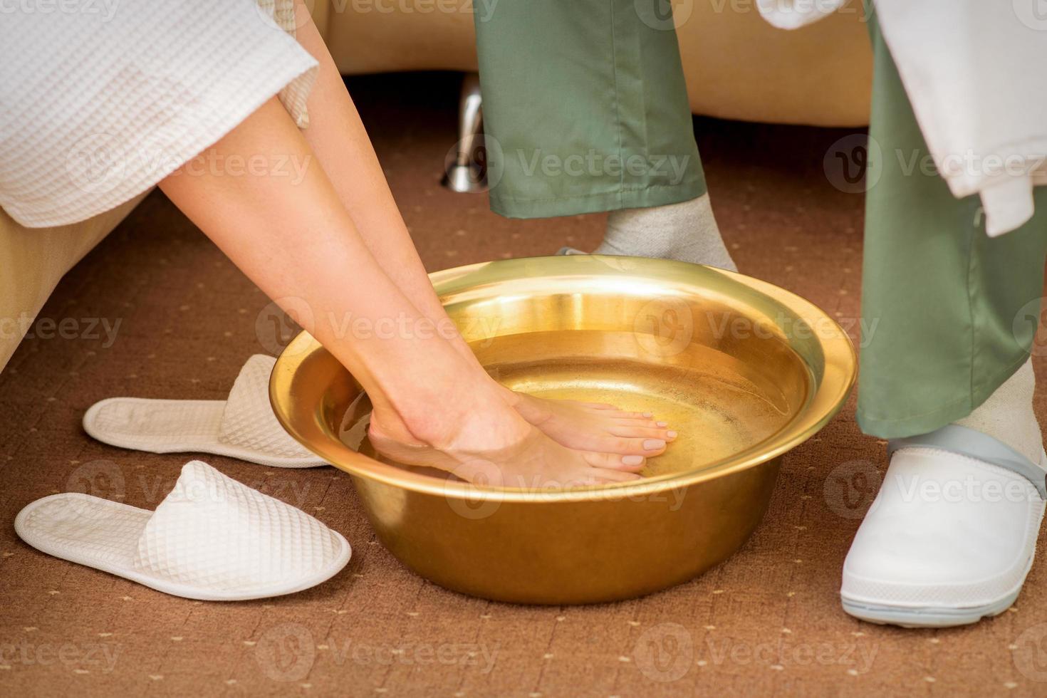 Female feet in a golden bowl with water in spa salon. Spa treatment. photo