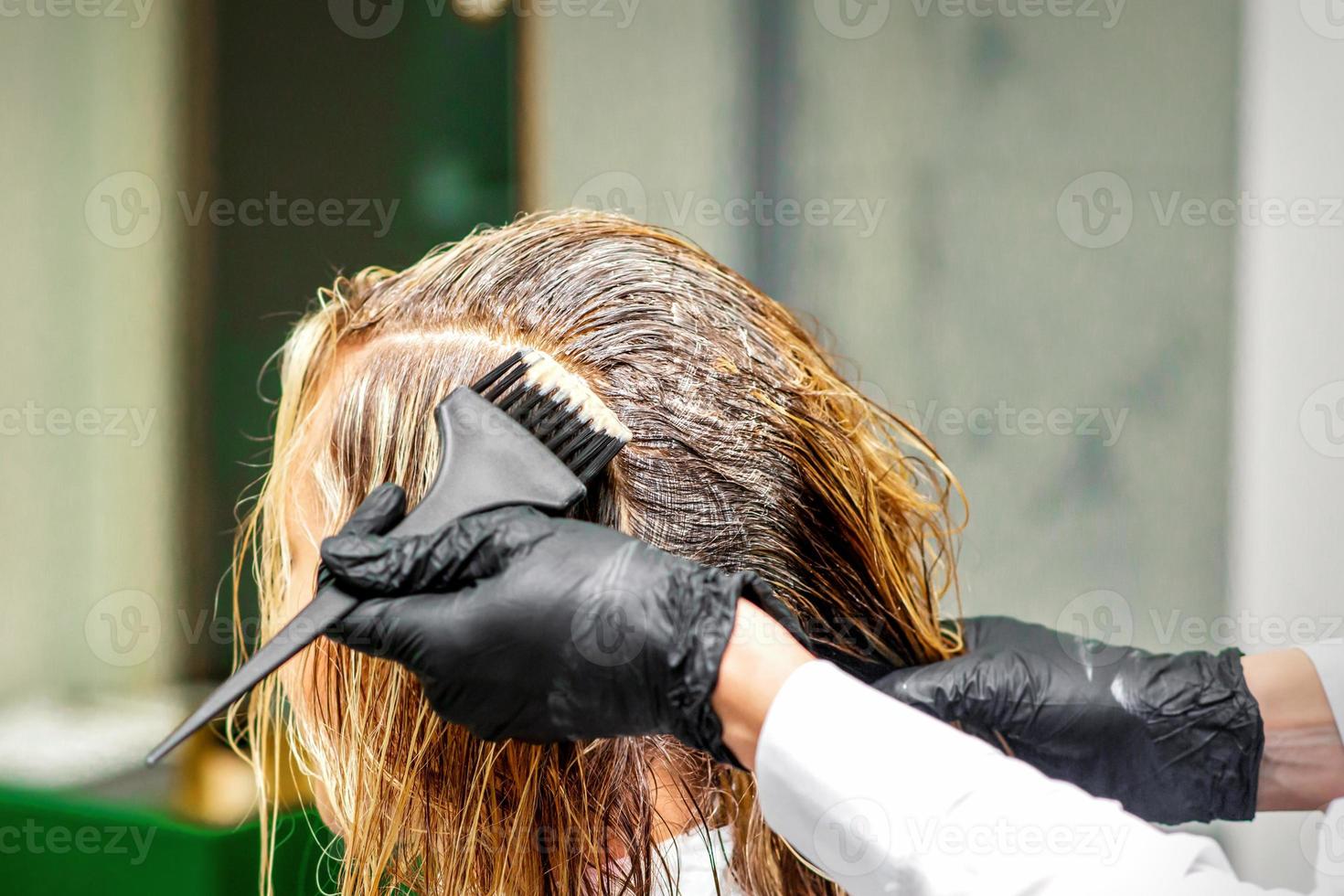 Hand of a hairdresser in black gloves applying dye to the female hair in a beauty salon. photo