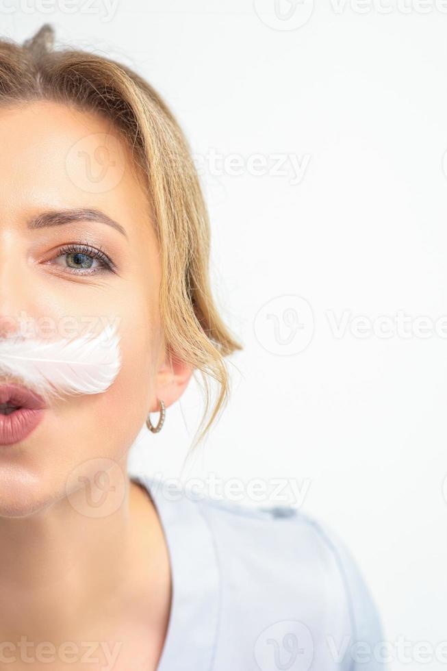 Funny beautician with a white feather-like mustache poses on white background, depilation concept. photo