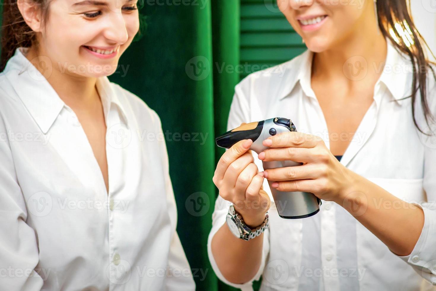 sonriente maquillaje artista muestra para su sonriente cliente aerógrafo herramienta dispositivo antes de aerógrafo procedimiento en un belleza salón. foto