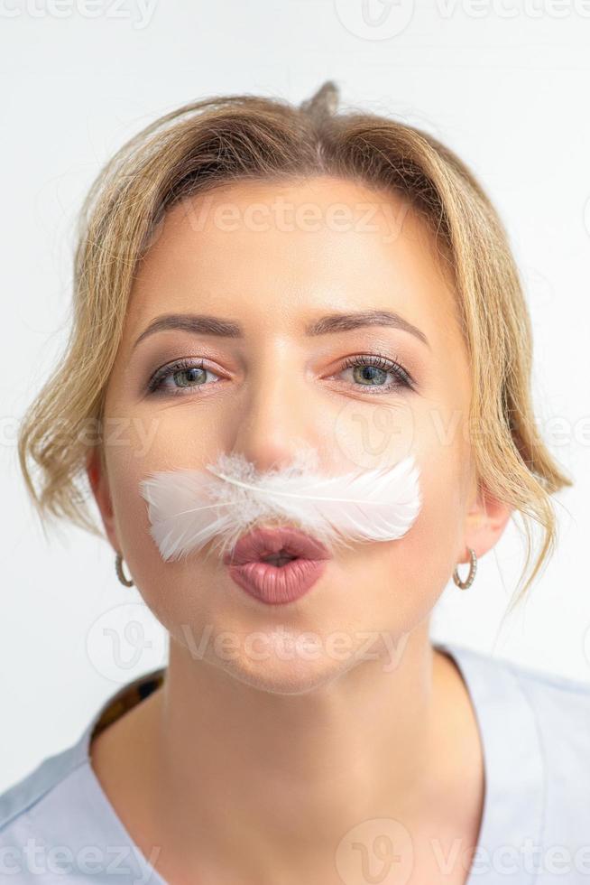 Funny beautician with a white feather-like mustache poses on white background, depilation concept. photo