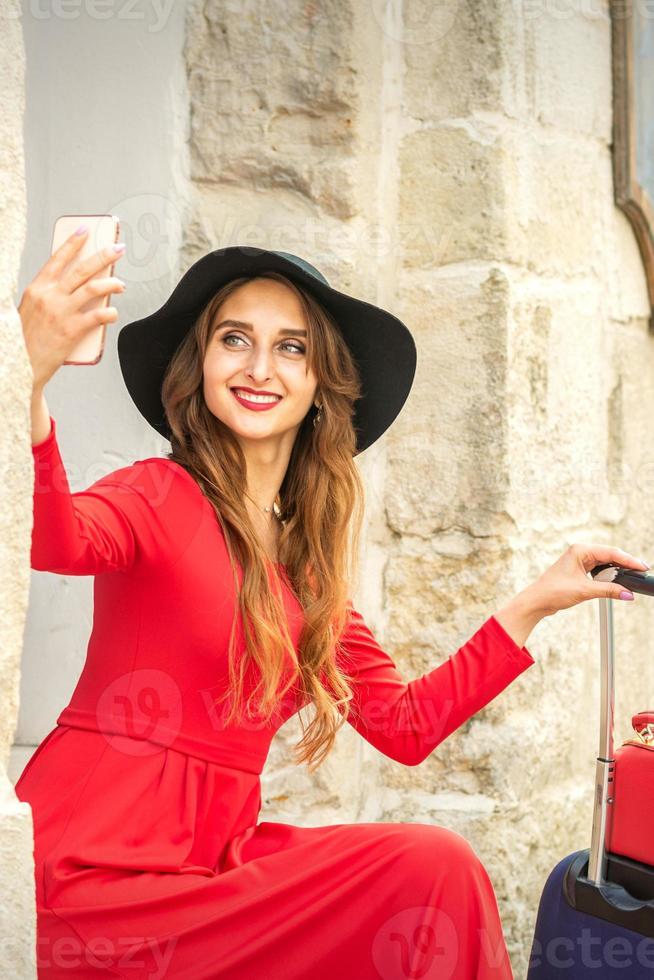 hermosa joven caucásico mujer en negro sombrero mirando en el teléfono inteligente sonriente y sentado en escalera a el puerta al aire libre. foto