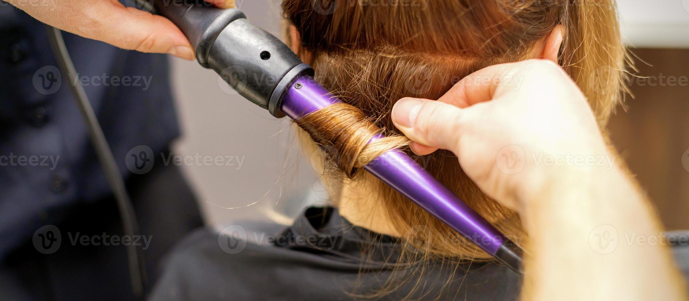 Close up of hairstylist's hands using a curling iron for hair curls in a beauty salon. photo