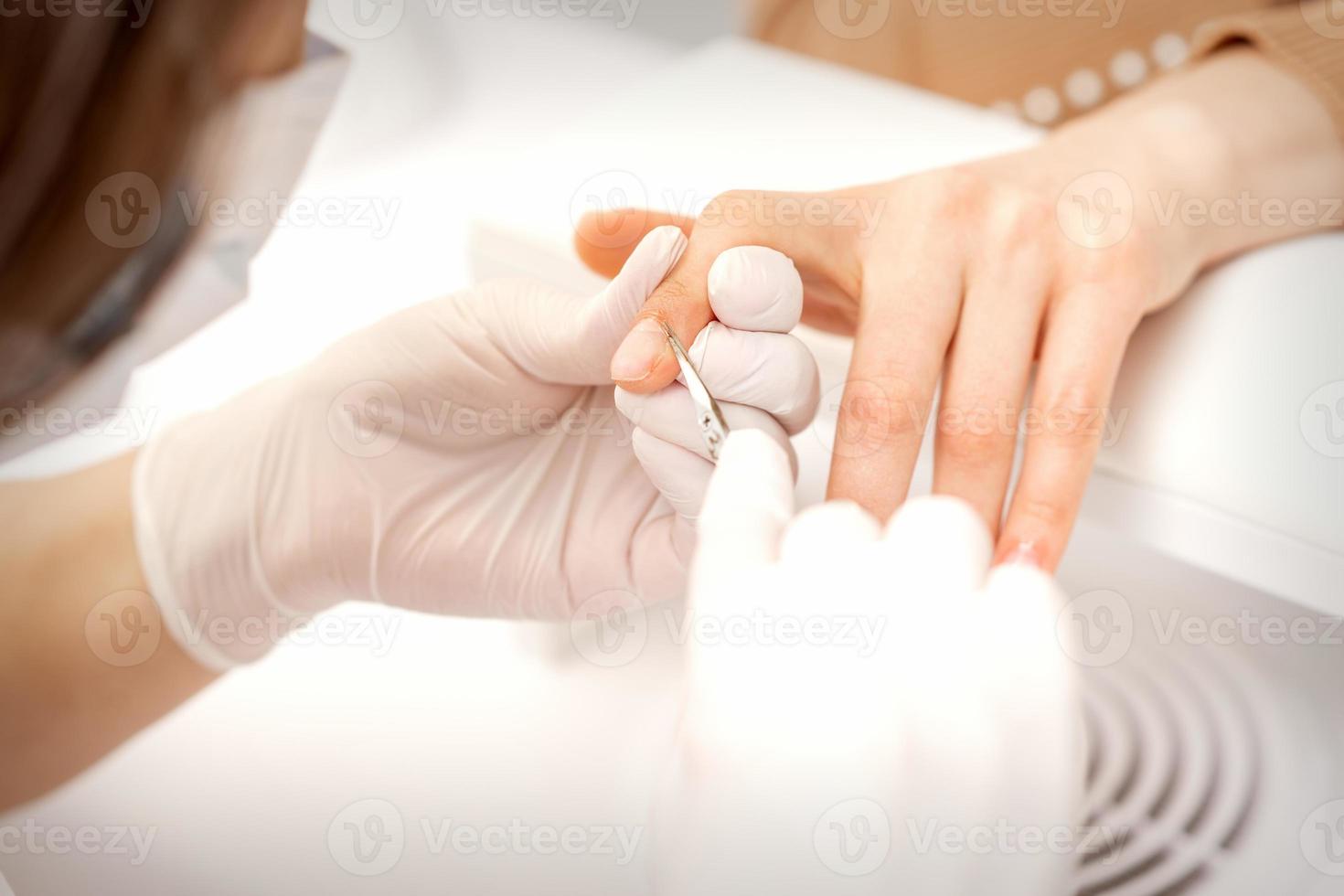 Close up of manicure master with manicure scissors removes cuticles of female nails at beauty salon. photo