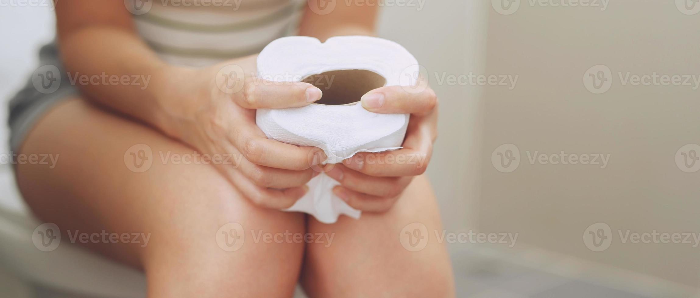 portrait of a woman suffers from diarrhea his stomach painful. ache and problem. hand hold tissue paper roll in front of toilet bowl. constipation in bathroom. Hygiene, health care concept. photo