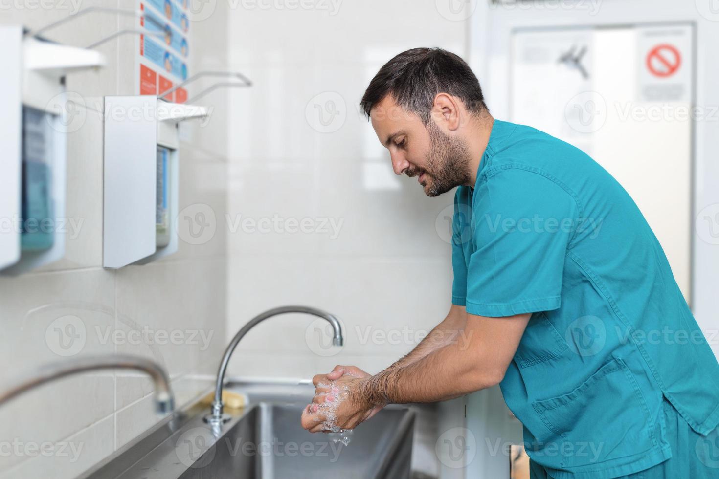 Doctor washing hands with soap. Male surgeon is preparing for surgery. He is in uniform at operating room. photo