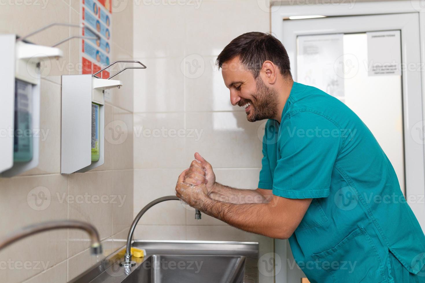 Doctor washing hands with soap. Male surgeon is preparing for surgery. He is in uniform at operating room. photo