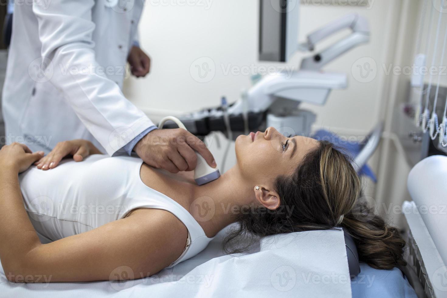 Man endocrinologist making ultrasonography to a female patient in an ultrasound office. Ultrasound diagnostics of the thyroid gland. photo