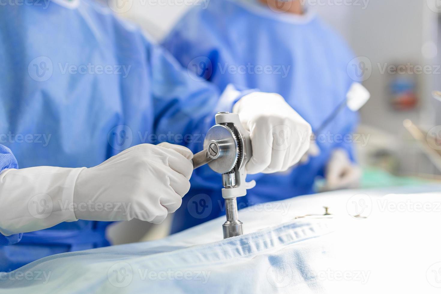 Surgeons hands close up performing surgery. Surgeon using drill machine during procedure. Doctors are wearing protective workwear in operating room. photo