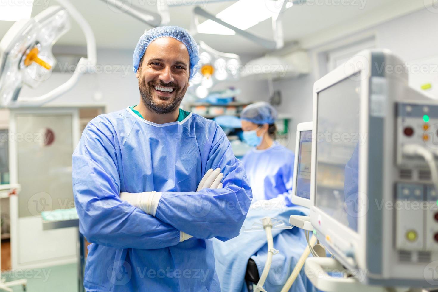 Anesthetist Working In Operating Theatre Wearing Protecive Gear checking monitors while sedating patient before surgical procedure in hospital photo
