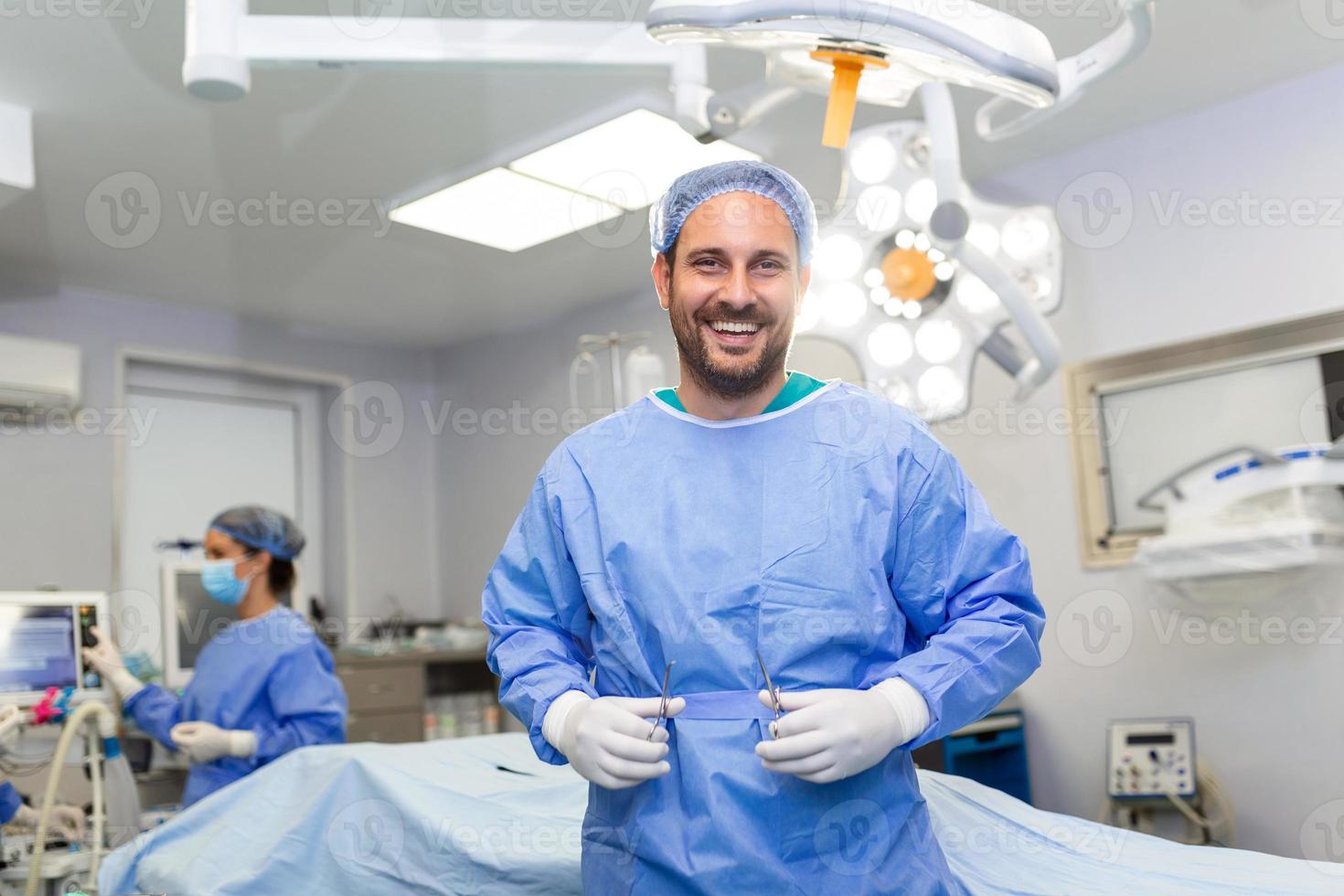 Portrait of male nurse surgeon OR staff member dressed in surgical scrubs gown mask and hair net in hospital operating room theater making eye contact smiling pleased happy looking at camera photo