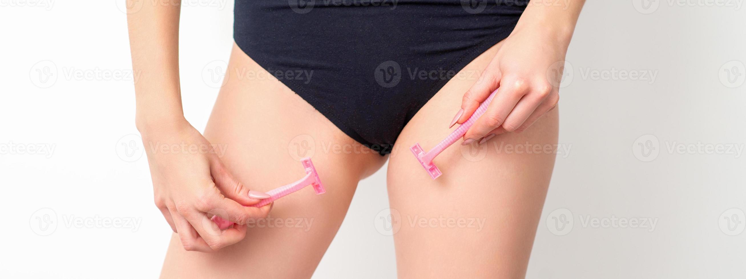 Young woman shaving crotch in bikini zone with two razors standing on white background, concept skincare and hair removal. photo
