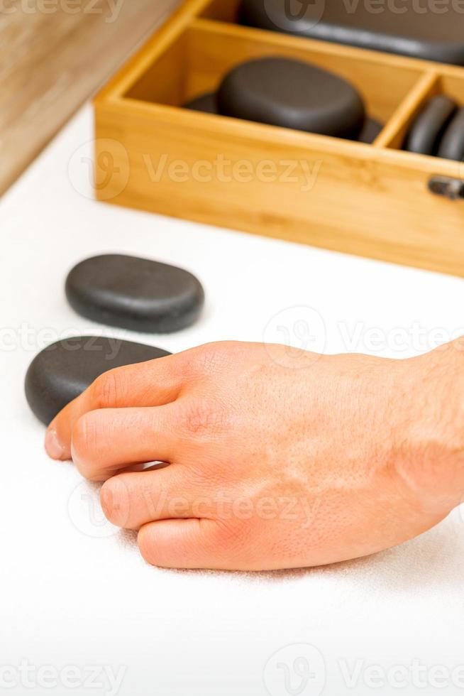 Hand of masseur takes black massage stones from the table in spa salon. photo