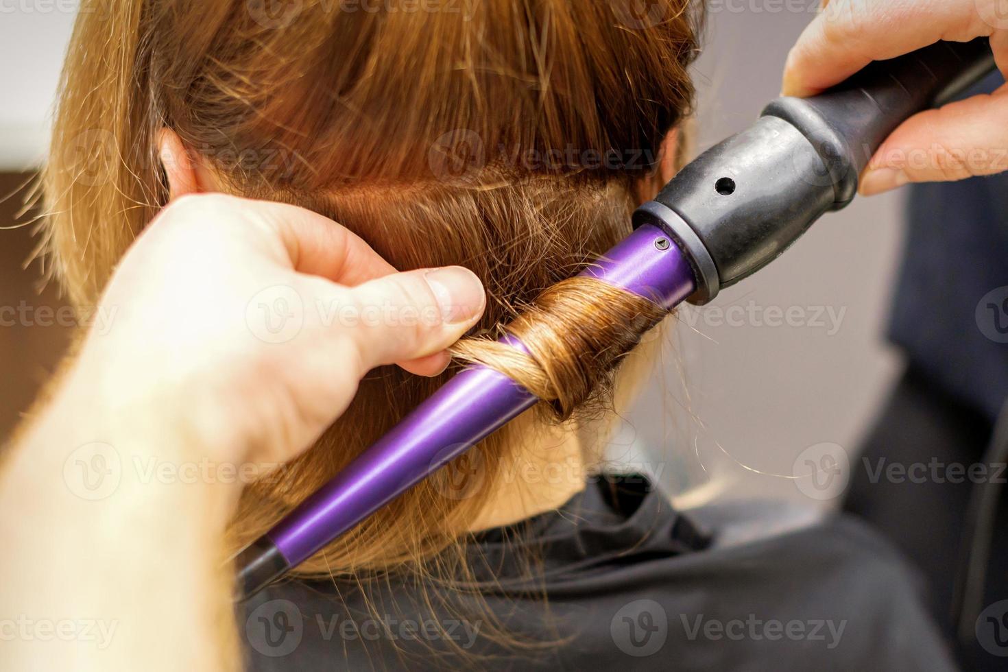 Close up of hairstylist's hands using a curling iron for hair curls in a beauty salon. photo