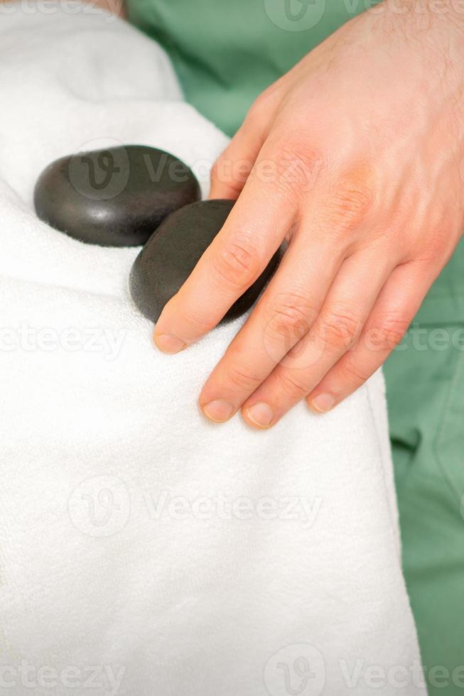 Close up of masseur's hand wipes black massage stones with a white towel. photo