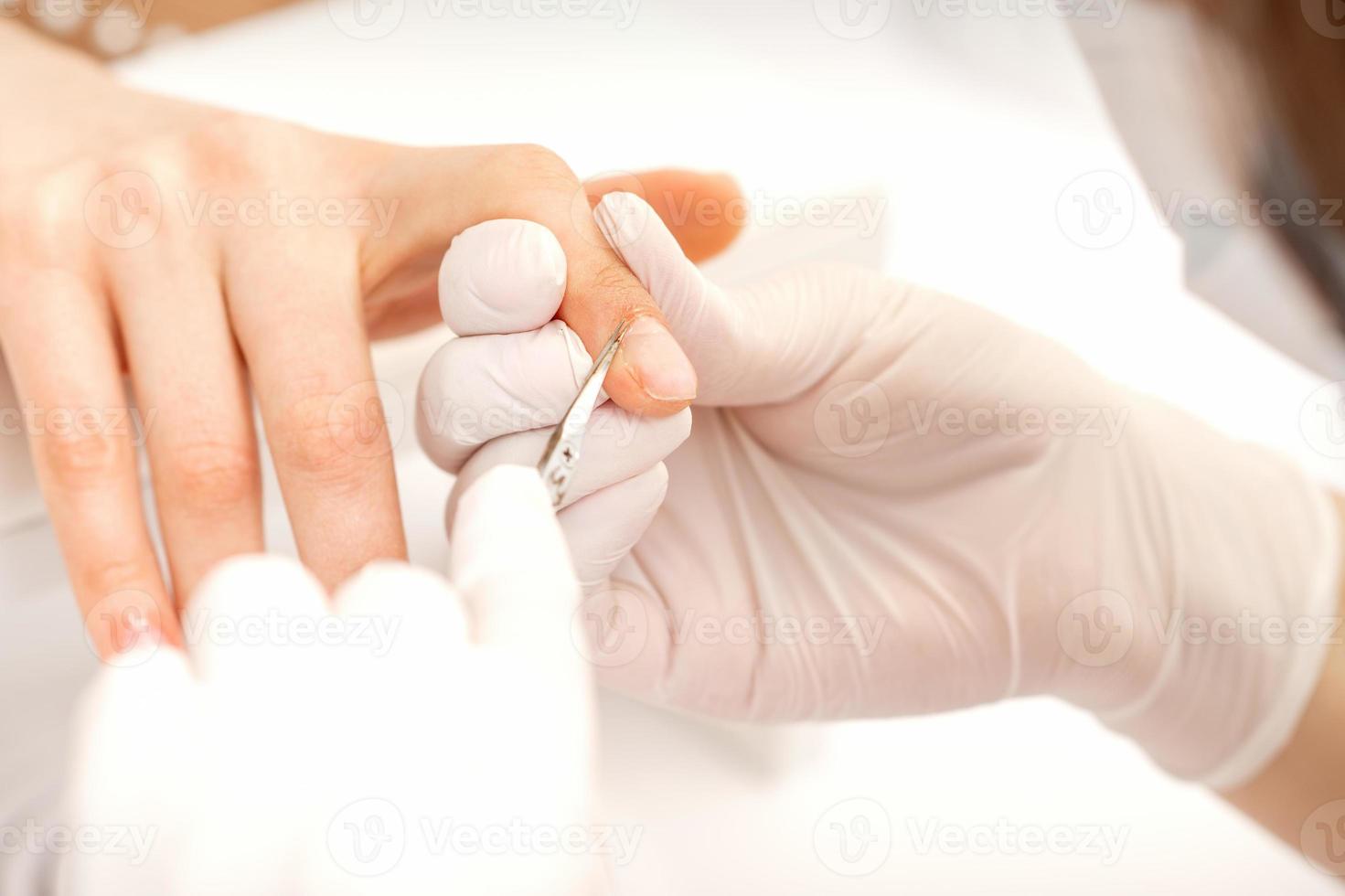 Close up of manicure master with manicure scissors removes cuticles of female nails at beauty salon. photo