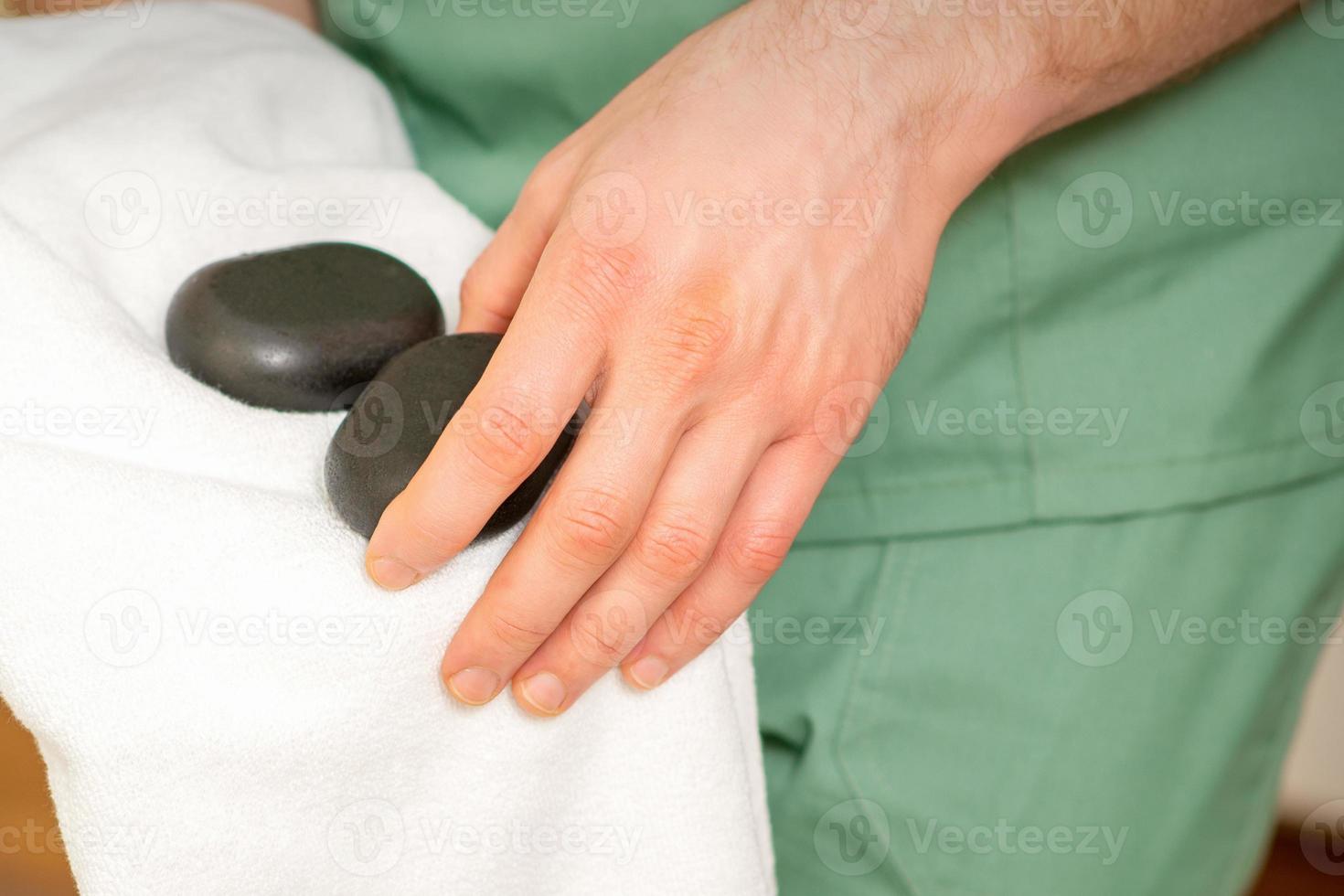 Close up of masseur's hand wipes black massage stones with a white towel. photo