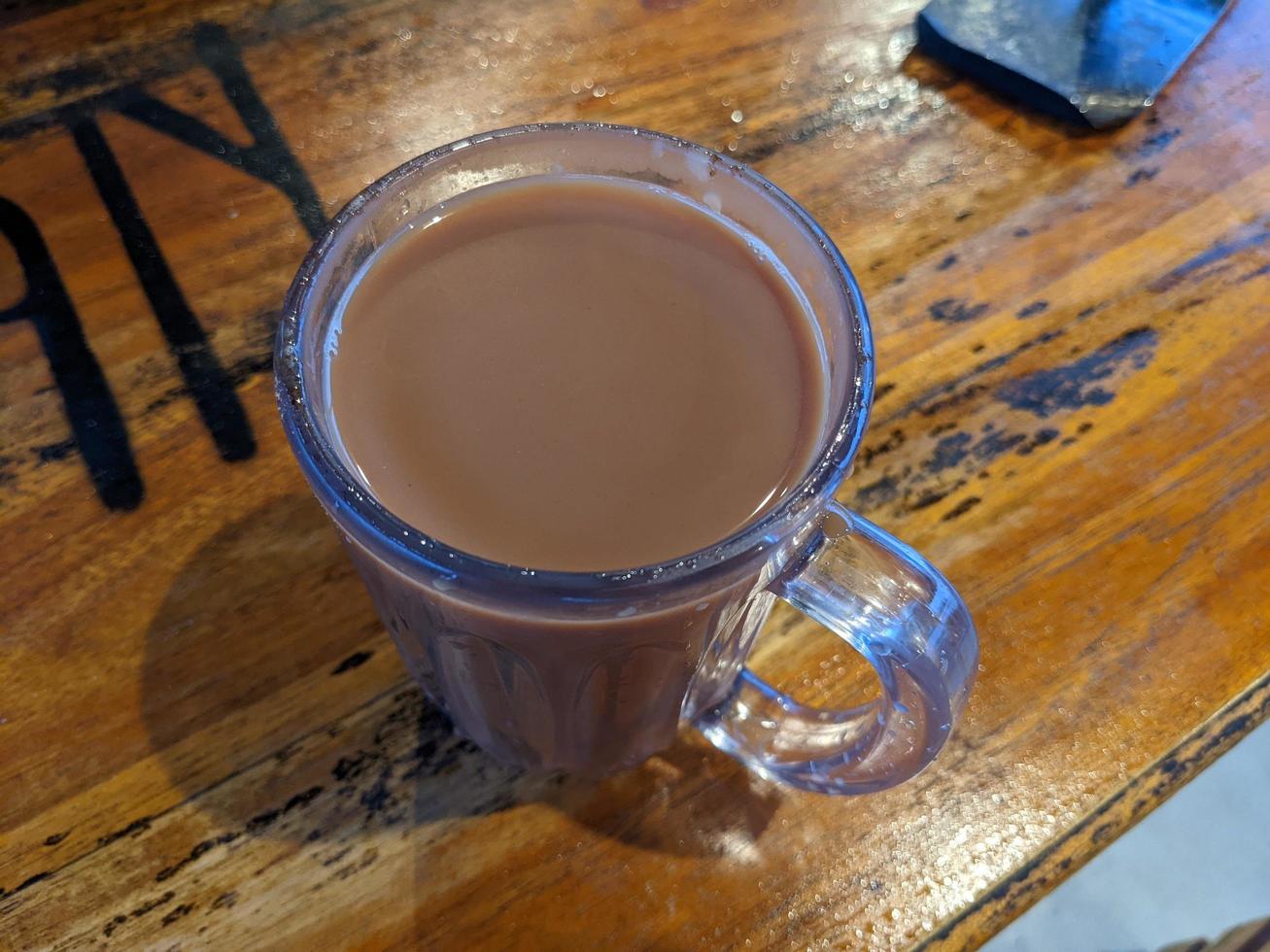 Close up photo of milk tea over the wooden table. The photo is suitable to use for coffee shop background, menu poster and coffee content media.