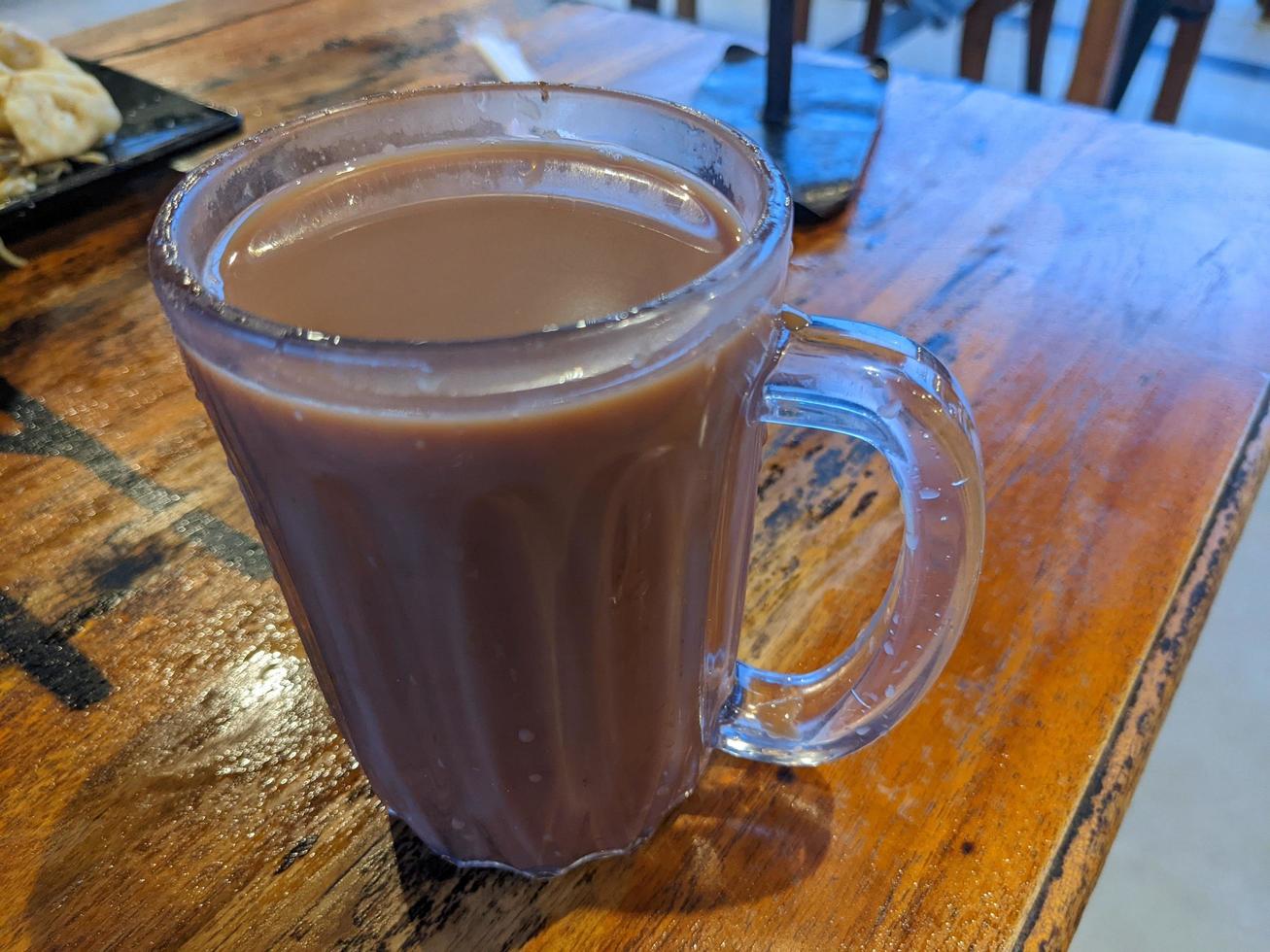 Close up photo of milk tea over the wooden table. The photo is suitable to use for coffee shop background, menu poster and coffee content media.