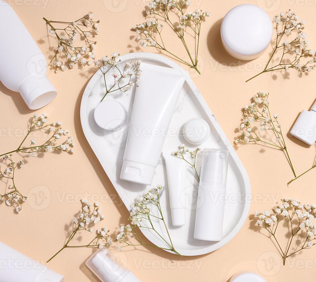 White plastic tubes, jars, and gypsophila branches on a beige background, containers for cosmetic creams and gels, advertising and brand promotion, top view photo