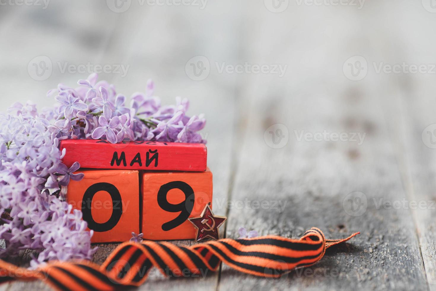 Wooden calendar with Russian text May 9, george ribbon and a bouquet of lilacs on a wooden background. Victory Day. Copy space. photo