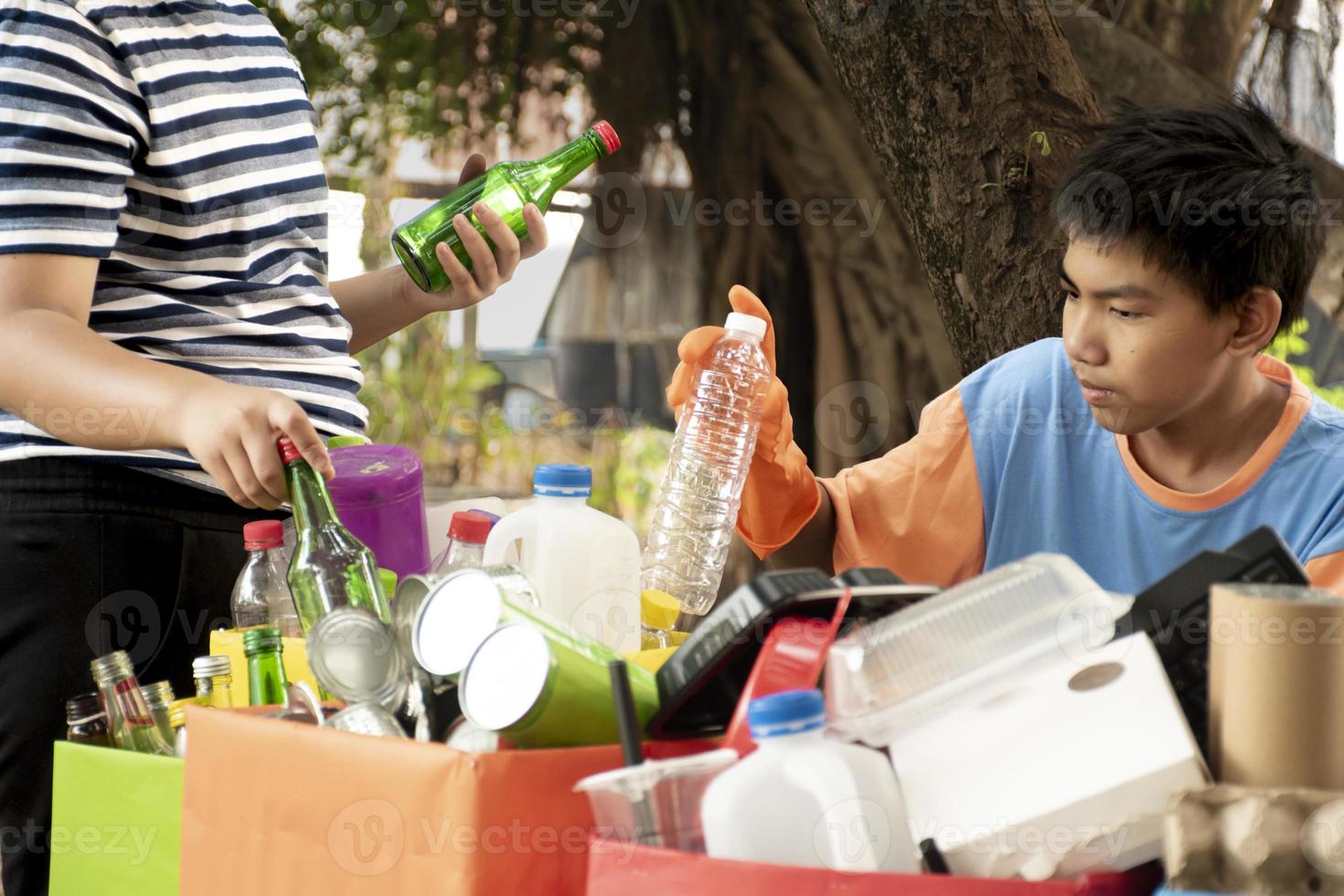 Young asian boy sorting various garbages and putting them into the boxes infront of him in the park, nature care and environment love concept. photo