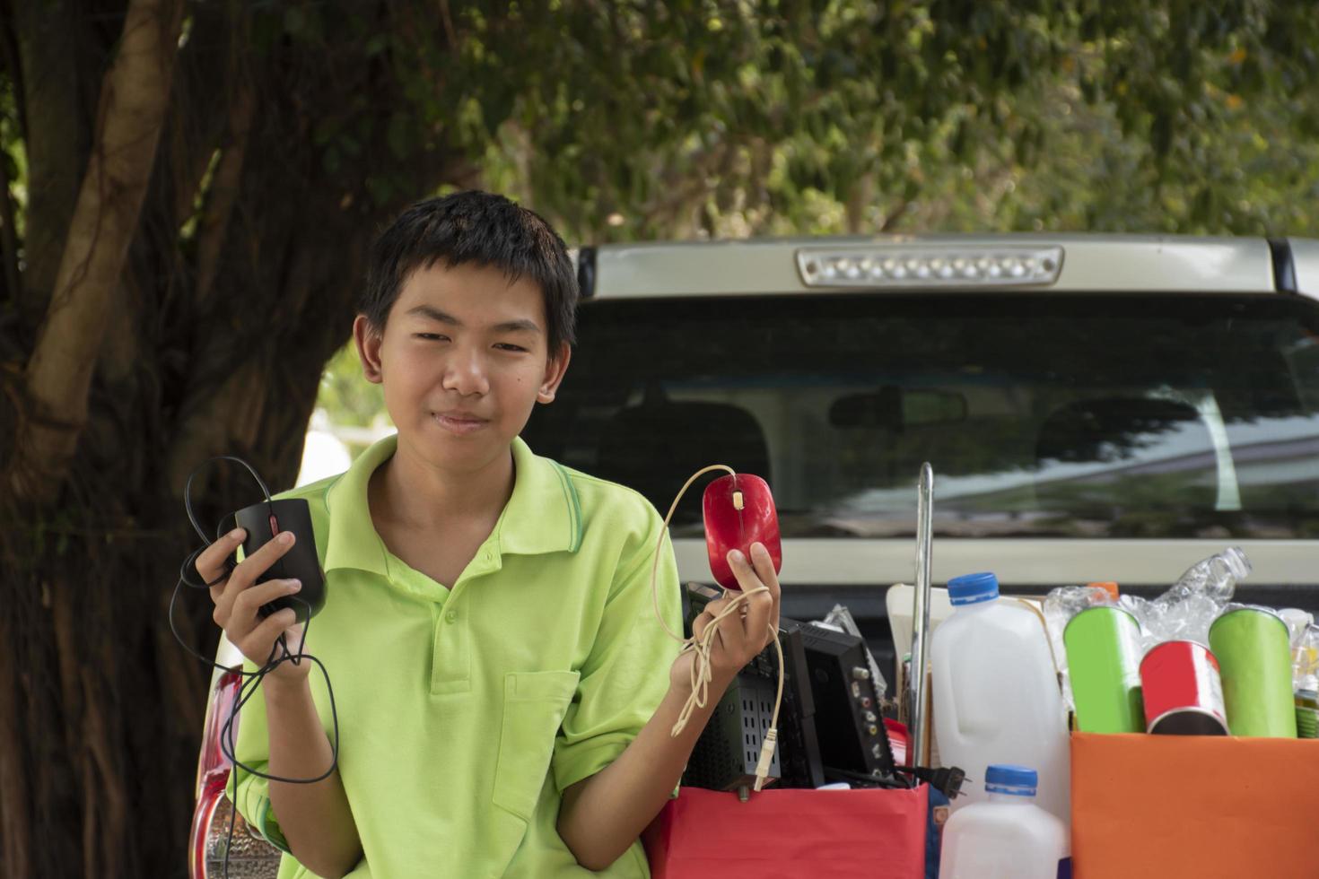 Asian boy in green t-shirt is separating different types of trash into color-coded boxes in the back of a pickup truck before leading them to sell and generate income after their school holidays. photo