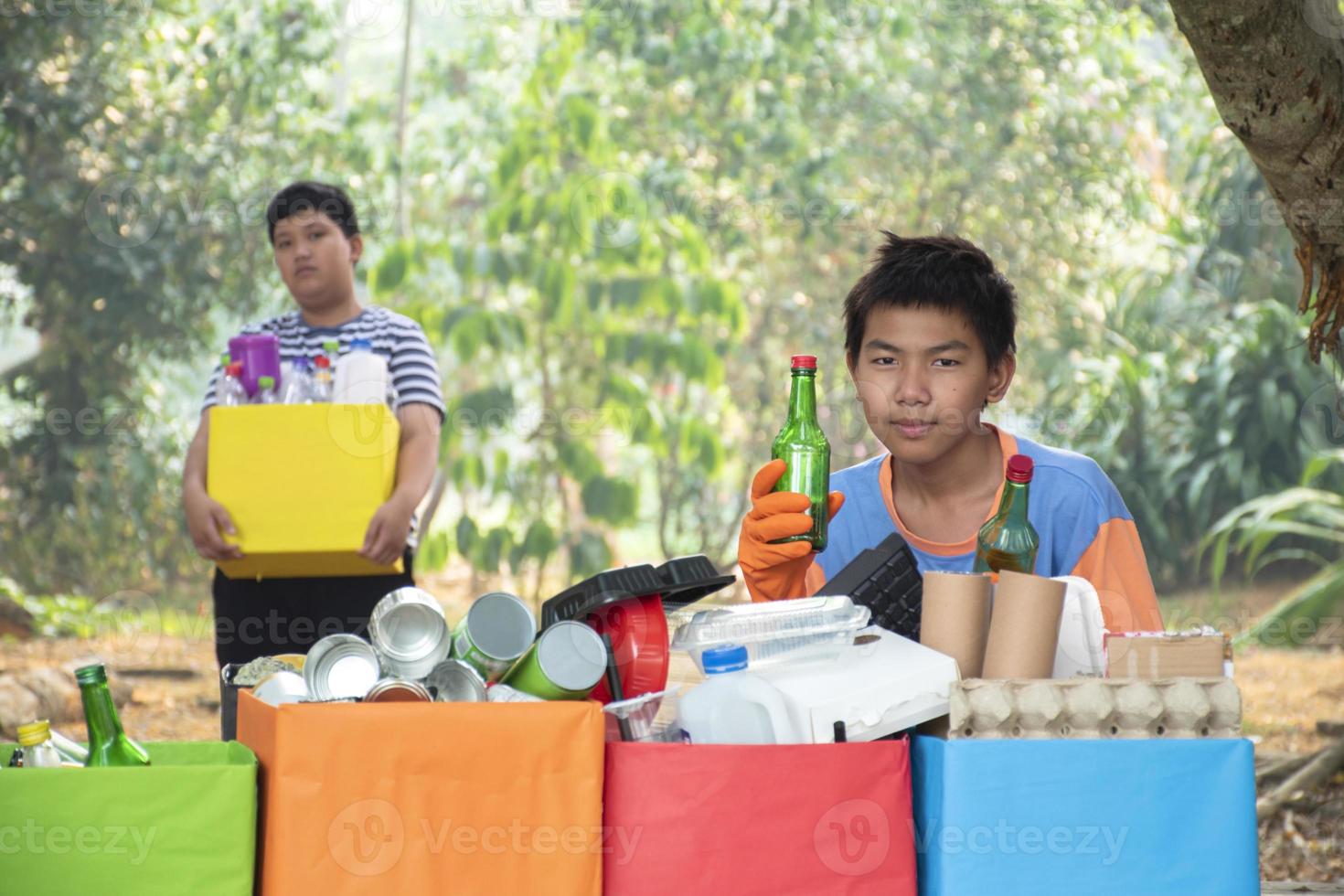 Young asian boy sorting various garbages and putting them into the boxes infront of him in the park, nature care and environment love concept. photo