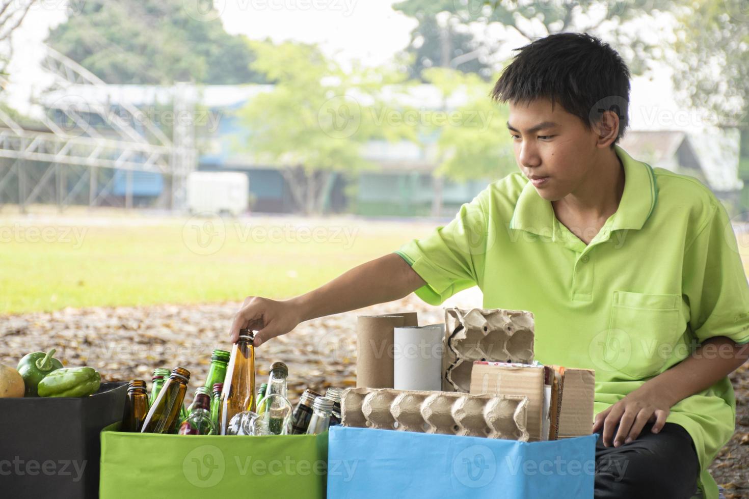 Young asian boy sorting various garbages and putting them into the boxes infront of him in the park, nature care and environment love concept. photo