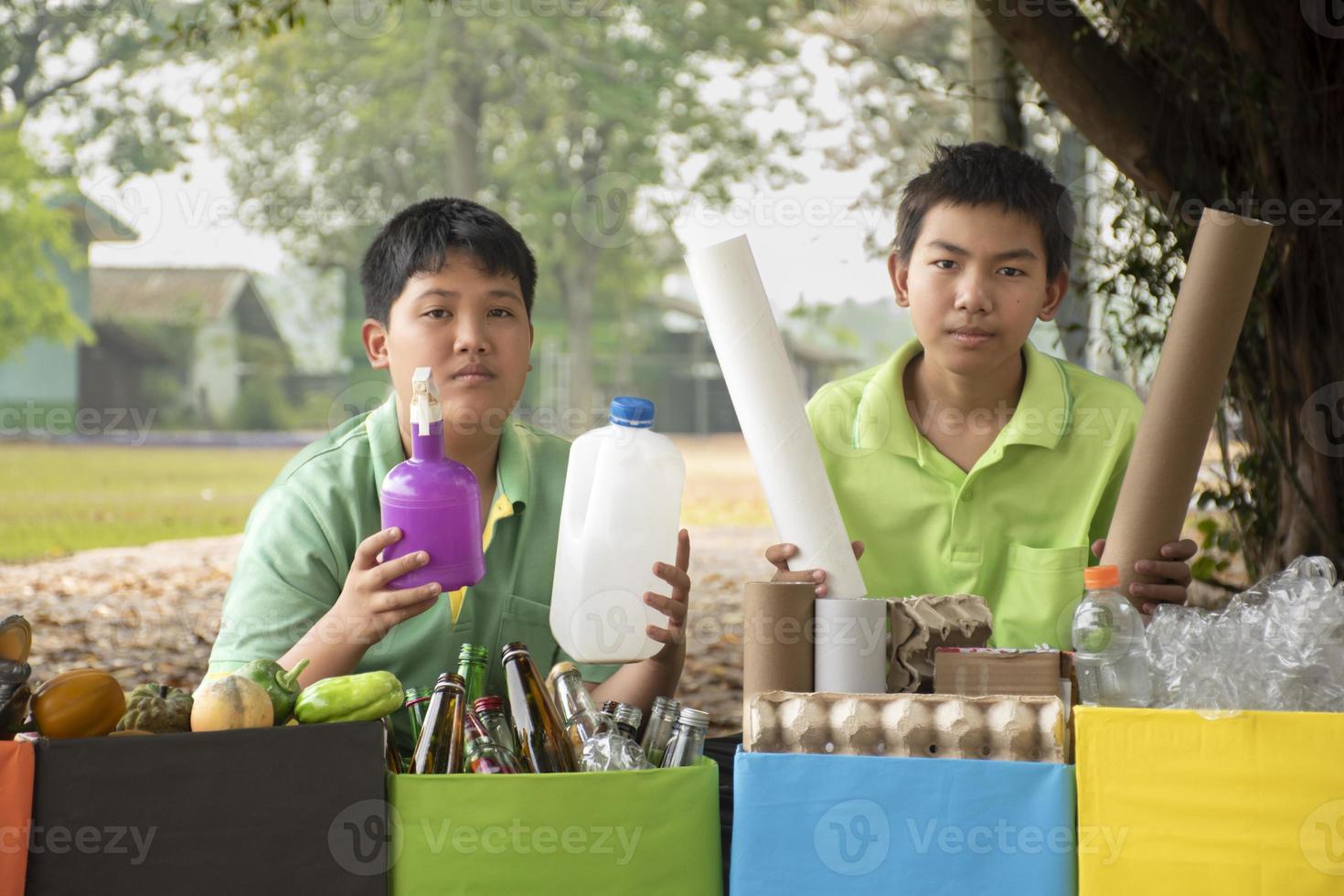 Young asian boy sorting various garbages and putting them into the boxes infront of him in the park, nature care and environment love concept. photo