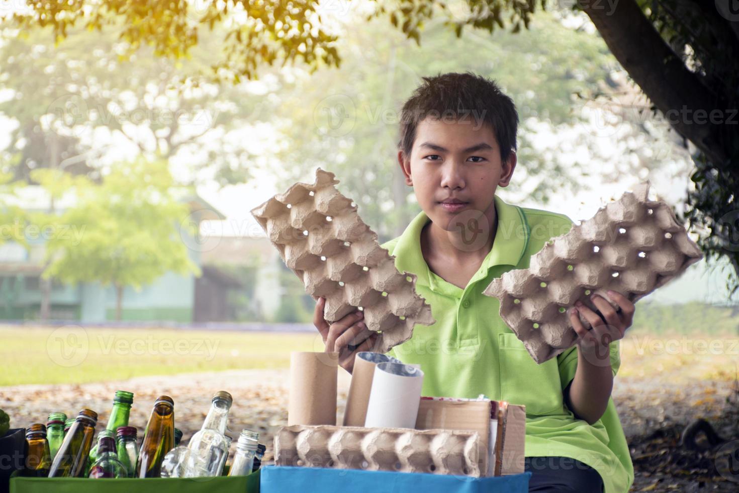 Young asian boy sorting various garbages and putting them into the boxes infront of him in the park, nature care and environment love concept. photo