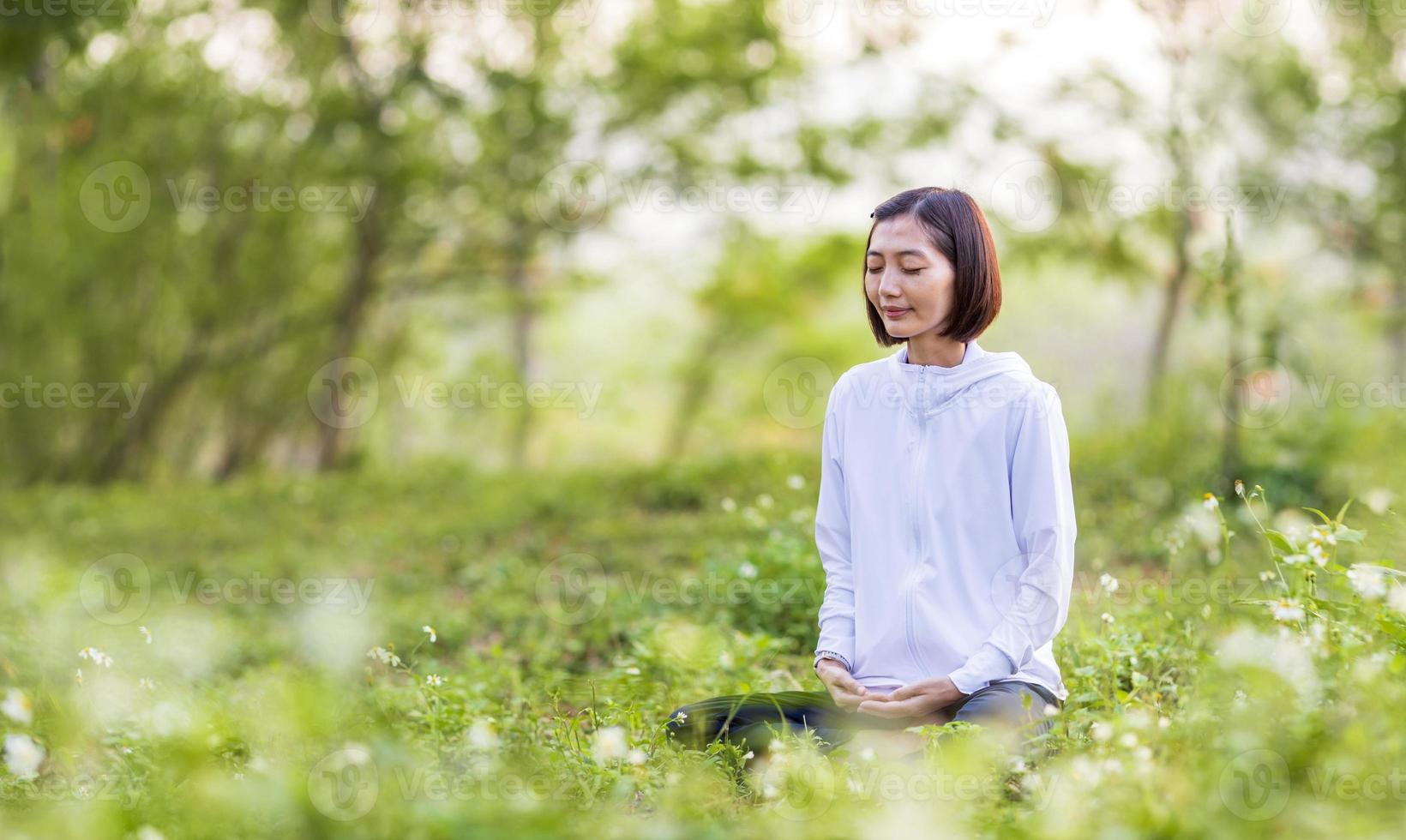 asiático mujer es relajantemente practicando meditación yoga en bosque lleno de margarita flor en verano a alcanzar felicidad desde interior paz sabiduría con Mañana ligero para sano mente y alma concepto foto